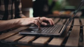 Close up view of freelance man typing on the laptop while sitting at the wooden table, video in the slow motion
