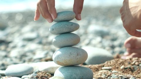 Woman hand building pebbles tower on beach during holidays. Macro of human hand making tower from pebbles on seashore. Relax on sea beach at summer vacations