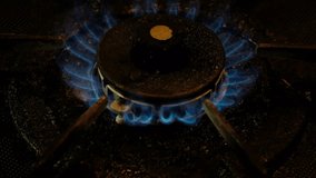 Blue fire on old dirty stove's burner in a dark kitchen. Tilt up footage.