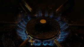 Blue fire on old dirty stove's burner in a dark kitchen. Tilt down footage.