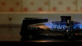 Blue fire on old dirty stove's burner in a dark kitchen. Panning to the right footage.