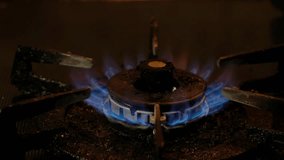 Blue fire on old dirty stove's burner in a dark kitchen. Panning to the left.