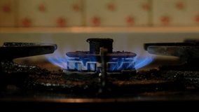 Blue fire on old dirty stove's burner in a dark kitchen. Panning to the left.