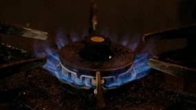 Blue fire on old dirty stove's burner in a dark kitchen. Tracking footage.