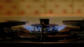 Blue fire on old dirty stove's burner in dark kitchen. Tracking shot.