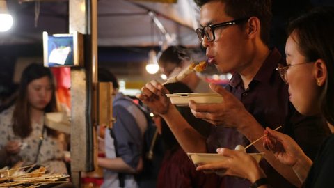 Young Couple Eating Traditional Asian Street Food Barbecue Satay on Wooden Stick at Night Market. 4K Cinematic Slowmotion Footage. 30 JAN 2019 - Kuala Lumpur, Malaysia.