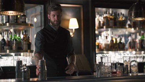 Attractive bartender professionally juggling cups and doing a show in beautiful modern bar. Slow motion