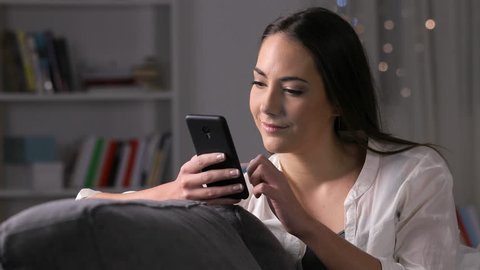 Happy girl using voice recognition on phone to record a message sitting on a couch in the night at home