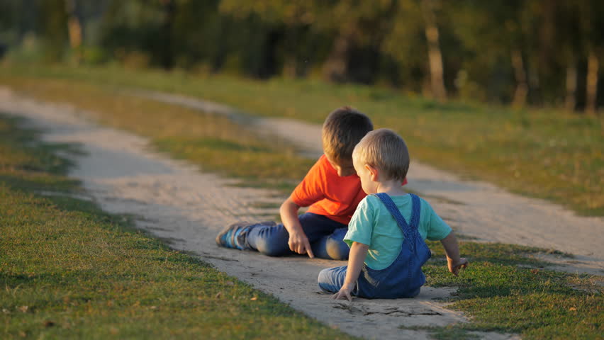 Baby child and elder brother play with dust on countryside road, family building memories, magical evening light