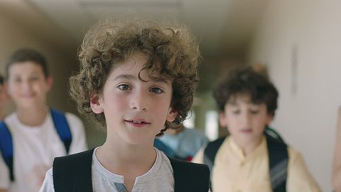 Close up portrait of beautiful , attractive , caucasian curly hair boy . Young boy looking and smiling on the camera inside school with friends . Portrait of children looks and smiles positive mood .