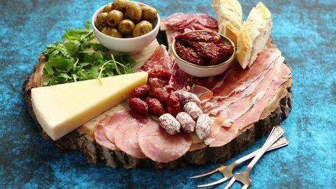 Delicious mix of different snacks and appetizers. Spanish tapas or italian antipasti on a wooden plate. View from above. Placed on blue table.