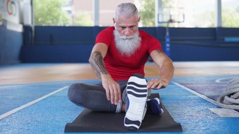 Senior hipster athlete doing stretching before training - Tattoo fitness man doing a workout session inside gym camp - Welness, trends and sport concept - Slow motion