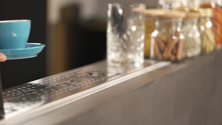 A hand holding a light blue cup on the sauce and putting it on the bar counter. Two hands are taking it away