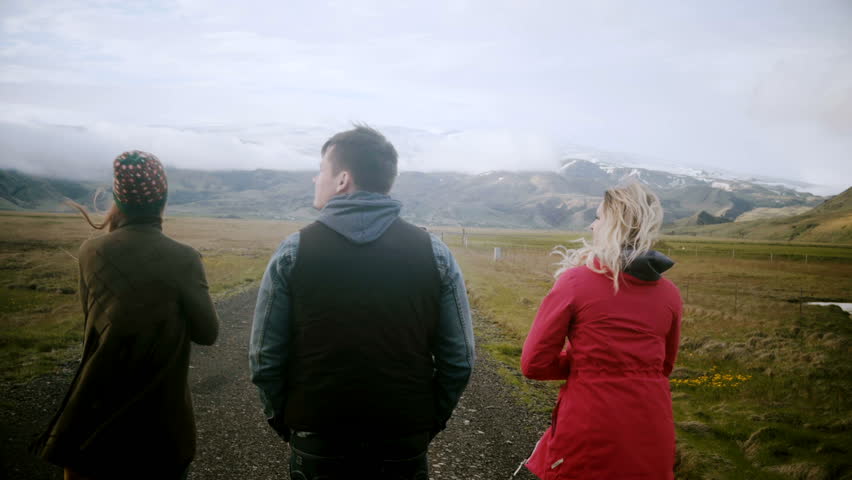 Back view group of young people walking on the road together and talking. Two women and man exploring Iceland together.