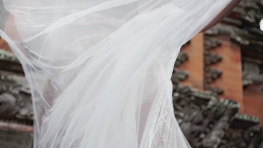 Beautiful bride posing near buddhist temple in Bali. Walking near by, waving veil. Romantic wedding. Tropical vacation.