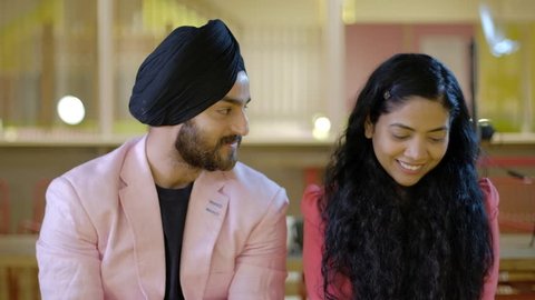 Beautiful Indian couple in love, turbaned Sikh and curly haired woman, talk in whispers as they smile, steal glances and feel generally embarrassed in front of the camera, naive and innocent 