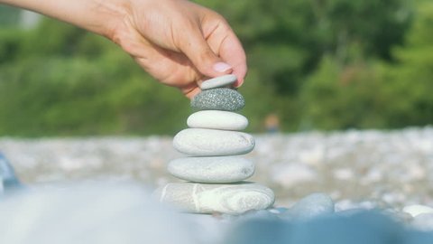 Hand making stone balance at sea beach. Closeup of pebbles stack at beach. Woman hand making pyramid from stones. Meditation on summer vacations. Spiritual harmony concept