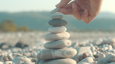 Stone balance closeup. Female hand making pebbles tower from sea stones. Macro of pyramid of pebbles on beach. Stack of stones on seashore. Meditation and relax on summer vacations concept