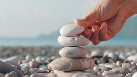 Hand making stone tower on sea beach. Close up of stack of balanced pebbles on beach. Woman making pyramid of stones for meditation at summer holidays