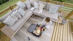 High angle view of girl packing suitcase at home on wooden patio outdoors. Woman  preparing luggage to go on vacations concept 