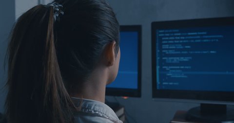 Young Woman Hacker Programmer working on computer at night, back side view