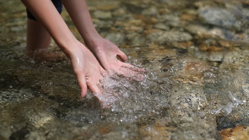 A girl playing and washing her hand with running stream from river. | Shutterstock HD Video #1023621982