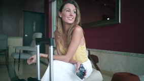 Smiling woman texting in hotel lobby with suitcase