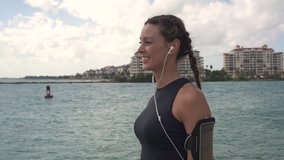 Sporty woman with headphones and armband smiling by waterfront