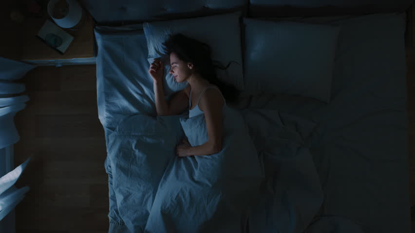Top View of Beautiful Young Woman Sleeping Cozily on a Bed in His Bedroom at Night. Blue Nightly Colors with Cold Weak Lamppost Light Shining Through the Window. | Shutterstock HD Video #1023631582