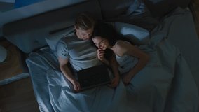 Cute Young Couple in Bed at Night Using Laptop, Watching Series, Reading Social Media, Browsing Through Internet, Talking and Having Fun. Top View Camera Shot - Powered by Shutterstock - Get 15% off with code: PIKWIZARD15