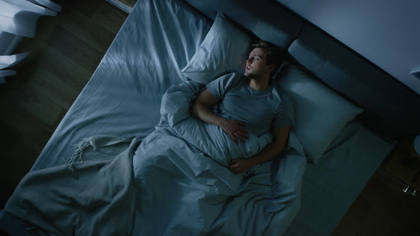 Top View of a Young Man in Bed at Night Having Terrible Nightmare, He Wakes Up Scared and Covered in Sweat. Zoom in Top View Camera Shot | Shutterstock HD Video #1023631702