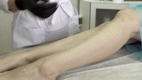 Epilation Master In Gloves Smears The Legs Of A Female Client Lying On A Couch With A Special Ointment To Protect The Skin. Concept Sugaring And Skin Care