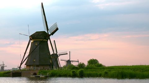 Magnificent scenery with row of old windmills near water pond or river and reeds slightly swaying in wind. Drainage system in Alblasserwaard polder, Knderdijk, Netherlands. Camera zooms out.
