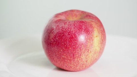 whole ripe pink apple fruit on white plate rotates on white background