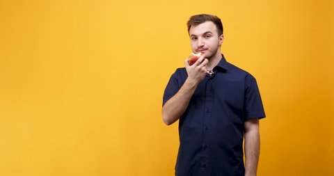 Handsome caucasian man enjoying an apple on yellow orange background in studio