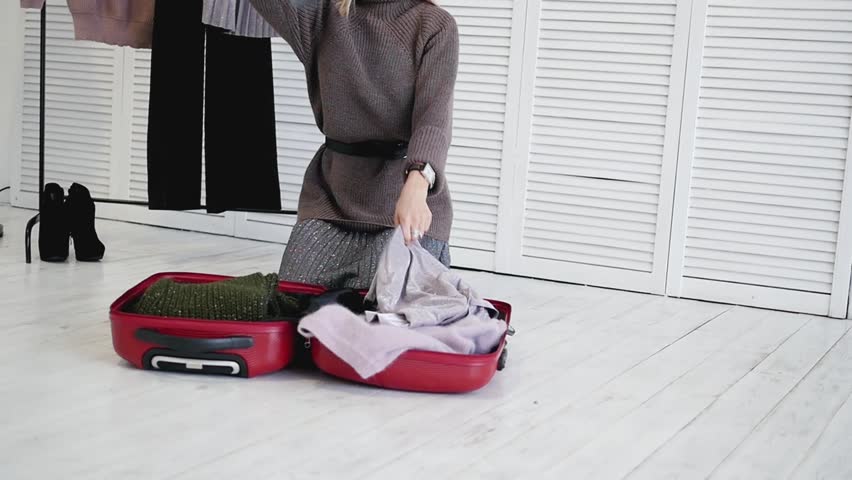 Top view of young girl sitting on wooden floor and unpacking clothes from trolley bag