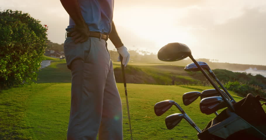 Handsome older golf stands on golf course with clubs, luxury golf detail shot, sunset ocean golf Royalty-Free Stock Footage #1023661621