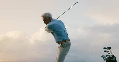 Tight shot of handsome older golfer swinging golf club with clouds, golfing in paradise, slow motion