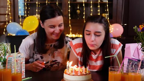 Happy teen girl and mother with birthday cake at anniversary party. Lighting candles on birthday cake. People celebrating birthday concept. Slow motion 4k hand held movement