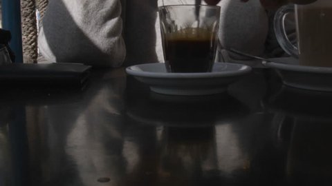 A hand stirring sugar into a coffee cup, outdoor closeup scene