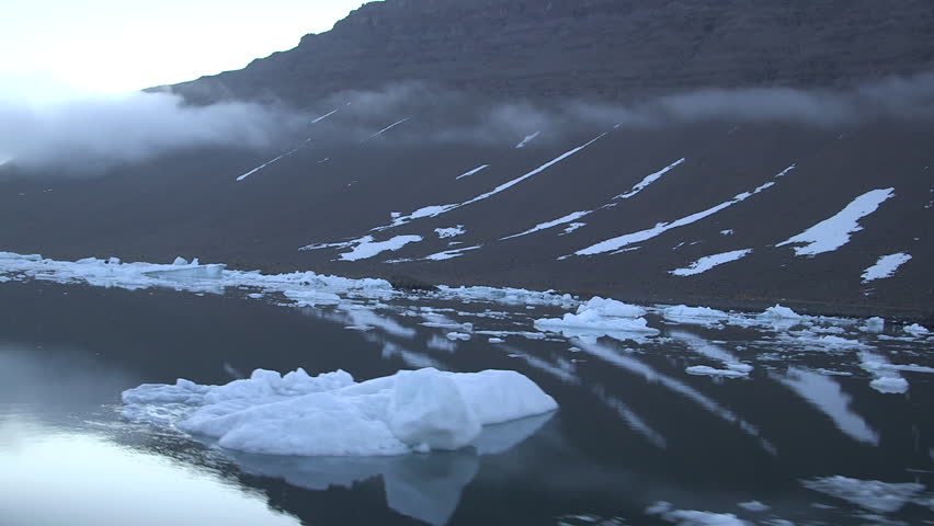 Moving shot from a boat of icebergs and misty coastal mountains in Greenland
