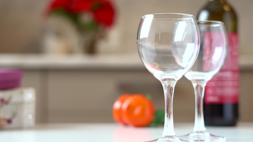 Man pours a great crimson wine in two glasses on a white table with natural light, domestic kitchen. 