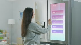 Beautiful Young Girl Walks Over to a Refrigerator While Drinking Her Morning Coffee. She is Checking the Weather Forecast and a To Do List on a Smart Fridge at Home. Kitchen is Bright and Cozy. - Powered by Shutterstock - Get 15% off with code: PIKWIZARD15