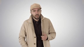 A positive bearded male dressed in a trench coat walking and talking on gradient background.