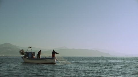 Two busy professional fishermen sailing on their boat across the sea with view of the Amalfi Coast in the background, on a bright sunny day. Wide shot on 8k helium RED camera.