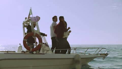 Group of friends partying on a boat together on the water with the Amalfi Coast in the background. Wide shot on 8k helium RED camera.