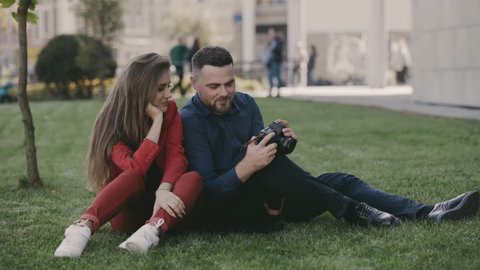 Smiling man and woman sitting on the lawn and watching photos. 4K