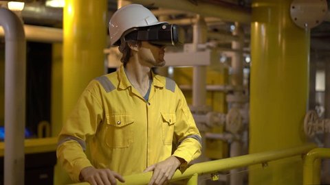 Young man in a yellow work uniform in industrial environment,oil Platform or liquefied gas plant uses VR glasses. Slowmotion shot