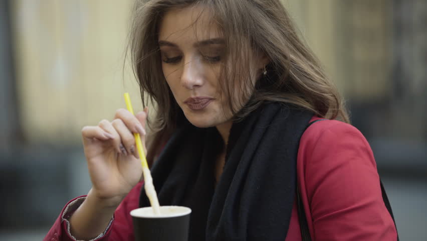 Happy girl drinks coffee in street cafe and smiles sincerely. 4K