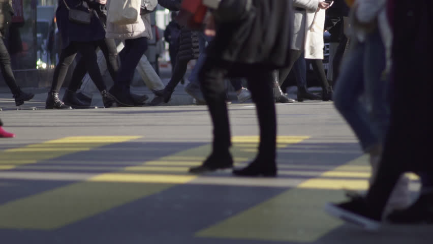Slow motion shot of many people carrying shopping bags while crossing a busy main street in Zürich city center on a cold and sunny winters day.